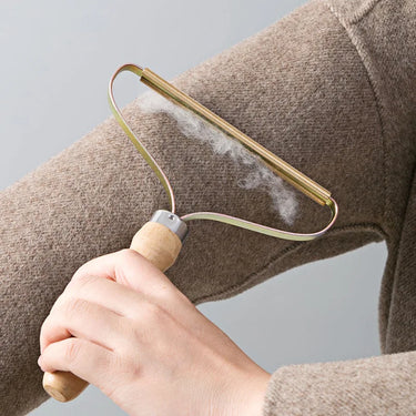 A hand uses the KittyNook Cat Co. Portable Pet Hair Lint Remover on a sweater, efficiently gathering pet hair and lint.